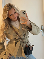 trench coat for women with a structured fit, high collar and dark buttons. Crafted from premium fabric, it highlights the waist and adds refined elegance to any autumn or winter outfit.