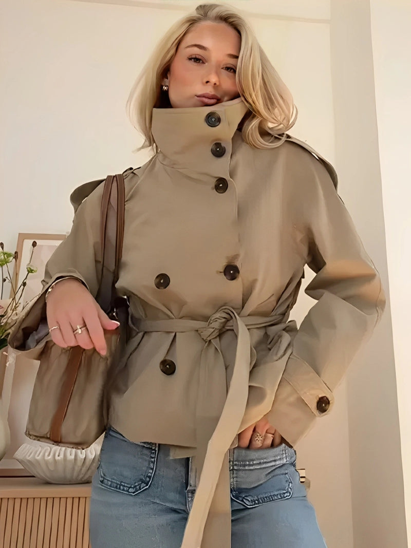 trench coat for women with a structured fit, high collar and dark buttons. Crafted from premium fabric, it highlights the waist and adds refined elegance to any autumn or winter outfit.