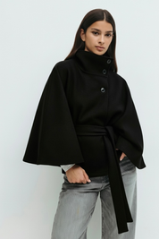High-Neck Belted Cape Jacket in camel wool blend. Poncho-inspired autumn/winter coat with high-neck collar, cape silhouette and adjustable waist belt. A chic belted jacket combining elegance, comfort and versatile seasonal style.