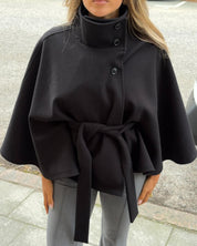 High-Neck Belted Cape Jacket in camel wool blend. Poncho-inspired autumn/winter coat with high-neck collar, cape silhouette and adjustable waist belt. A chic belted jacket combining elegance, comfort and versatile seasonal style.