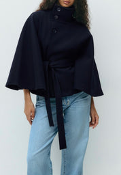 High-Neck Belted Cape Jacket in camel wool blend. Poncho-inspired autumn/winter coat with high-neck collar, cape silhouette and adjustable waist belt. A chic belted jacket combining elegance, comfort and versatile seasonal style.