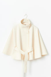 High-Neck Belted Cape Jacket in camel wool blend. Poncho-inspired autumn/winter coat with high-neck collar, cape silhouette and adjustable waist belt. A chic belted jacket combining elegance, comfort and versatile seasonal style.