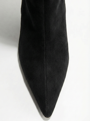 Black knee-high boot with a smooth suede-like finish, pointed toe, discreet low block heel, straight shaft design, and a slim metallic buckle detail at the top.