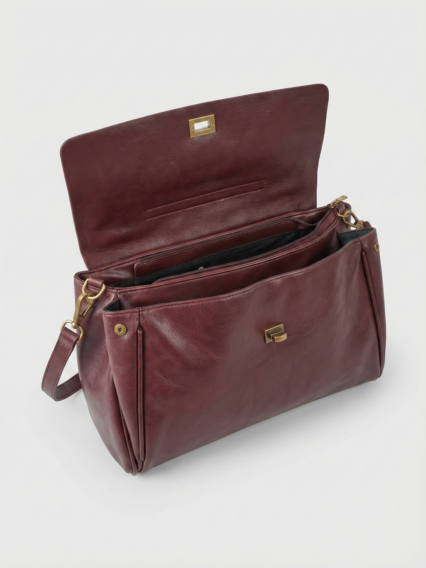 Burgundy leather shoulder bag with structured shape, flap closure and slim top handle, photographed on a light background