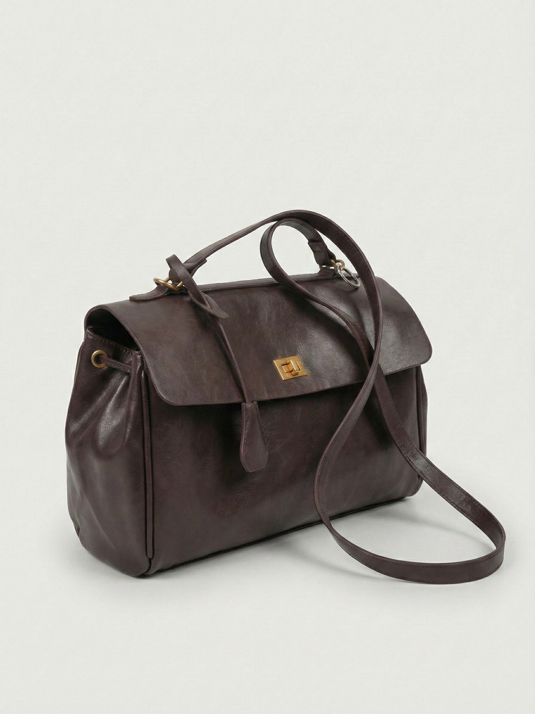 Dark brown leather shoulder bag with structured shape, flap closure and slim top handle, photographed on a light background