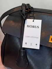 Black leather shoulder bag with structured shape, flap closure and slim top handle, photographed on a light background