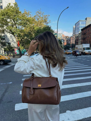 Brown leather shoulder bag with structured shape, flap closure and slim top handle, photographed on a light background
