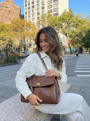 Brown leather shoulder bag with structured shape, flap closure and slim top handle, photographed on a light background