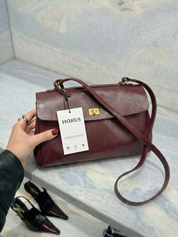 Burgundy leather shoulder bag with structured shape, flap closure and slim top handle, photographed on a light background