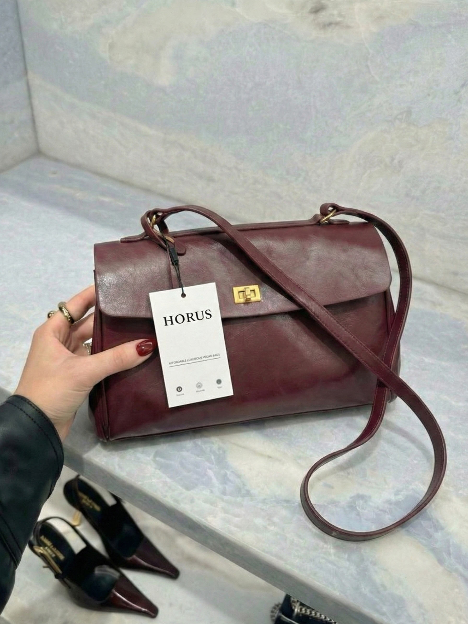 Burgundy leather shoulder bag with structured shape, flap closure and slim top handle, photographed on a light background