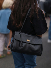 Black leather shoulder bag with structured shape, flap closure and slim top handle, photographed on a light background