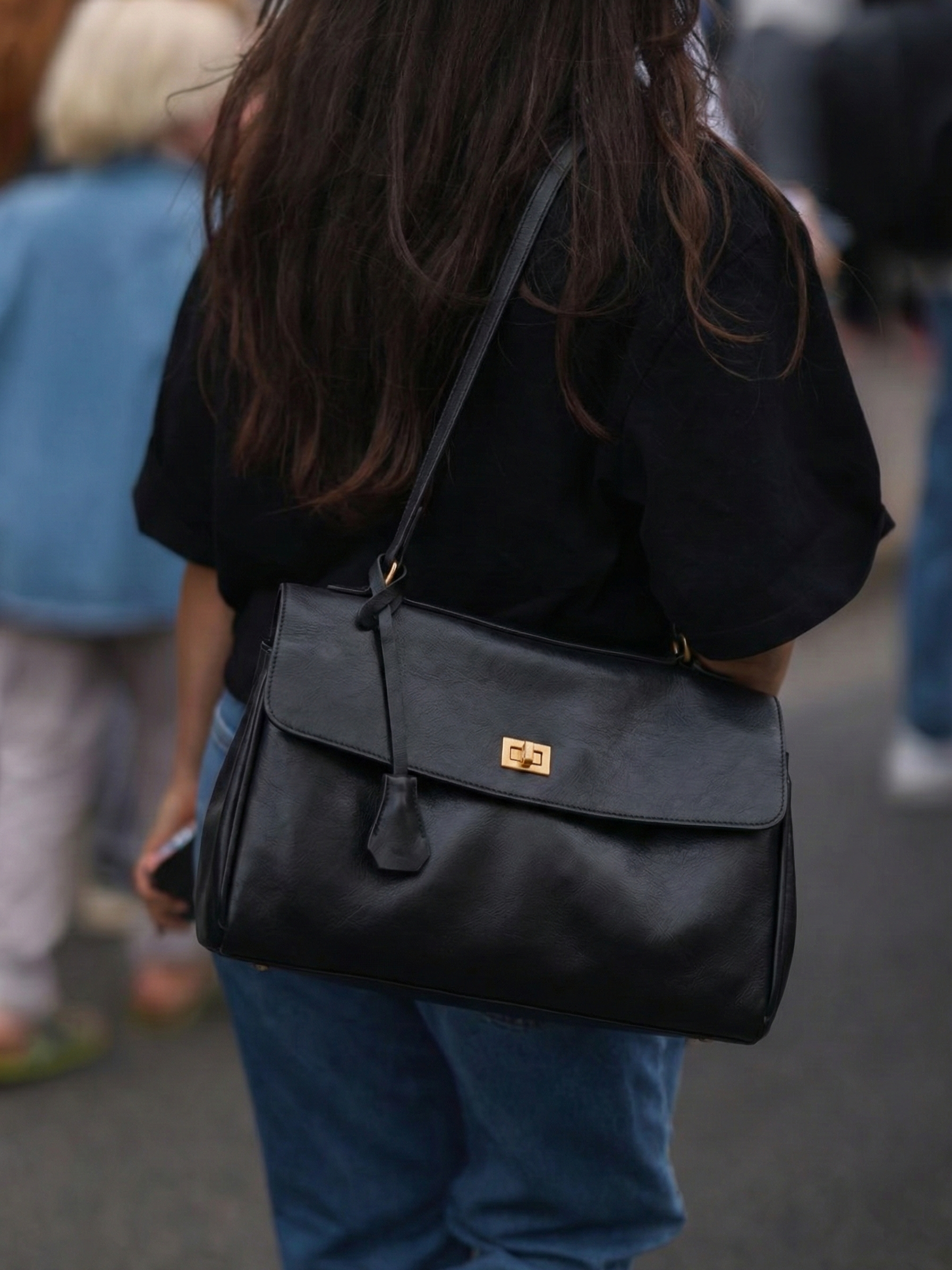 Black leather shoulder bag with structured shape, flap closure and slim top handle, photographed on a light background