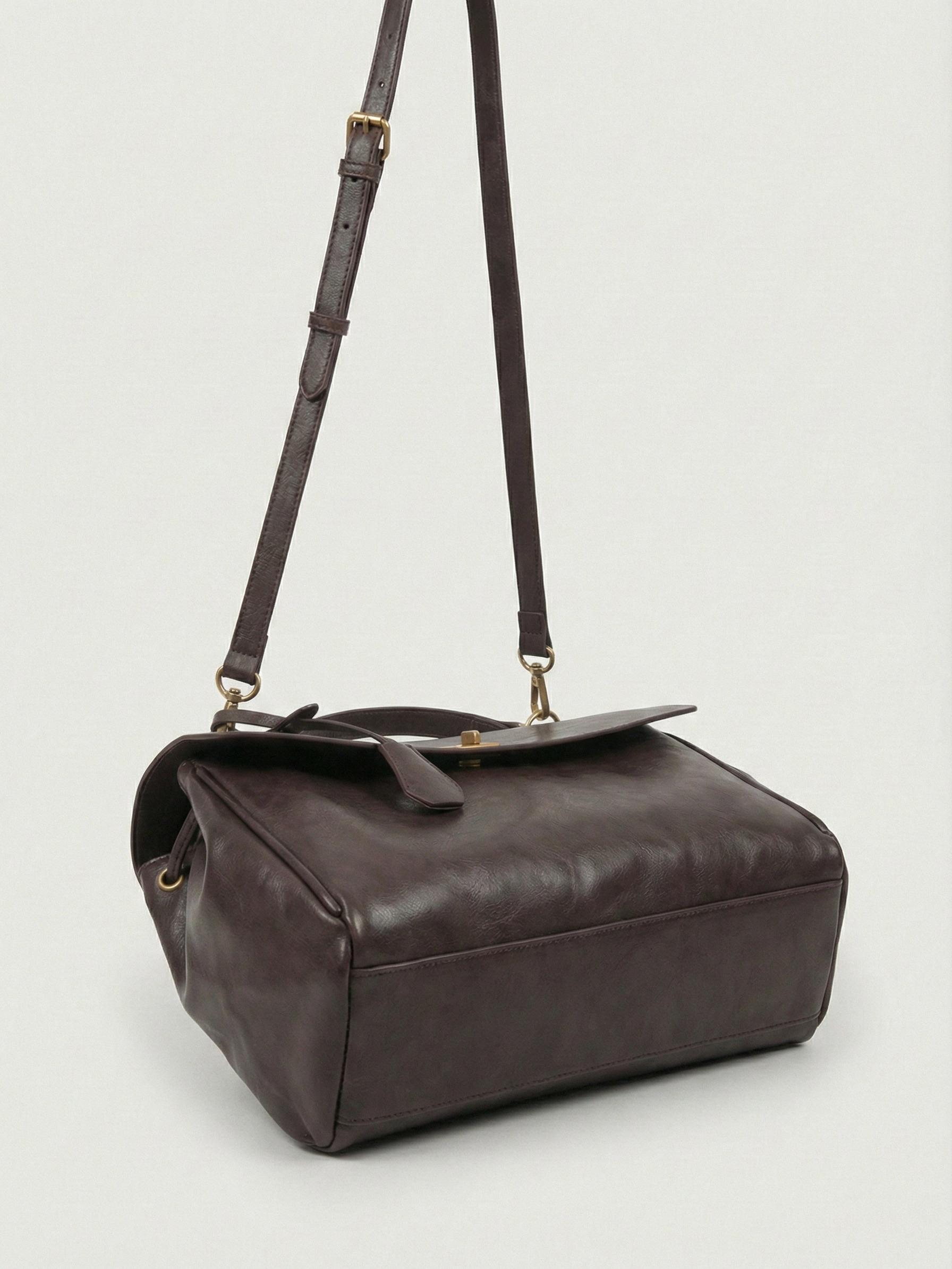 Dark brown leather shoulder bag with structured shape, flap closure and slim top handle, photographed on a light background
