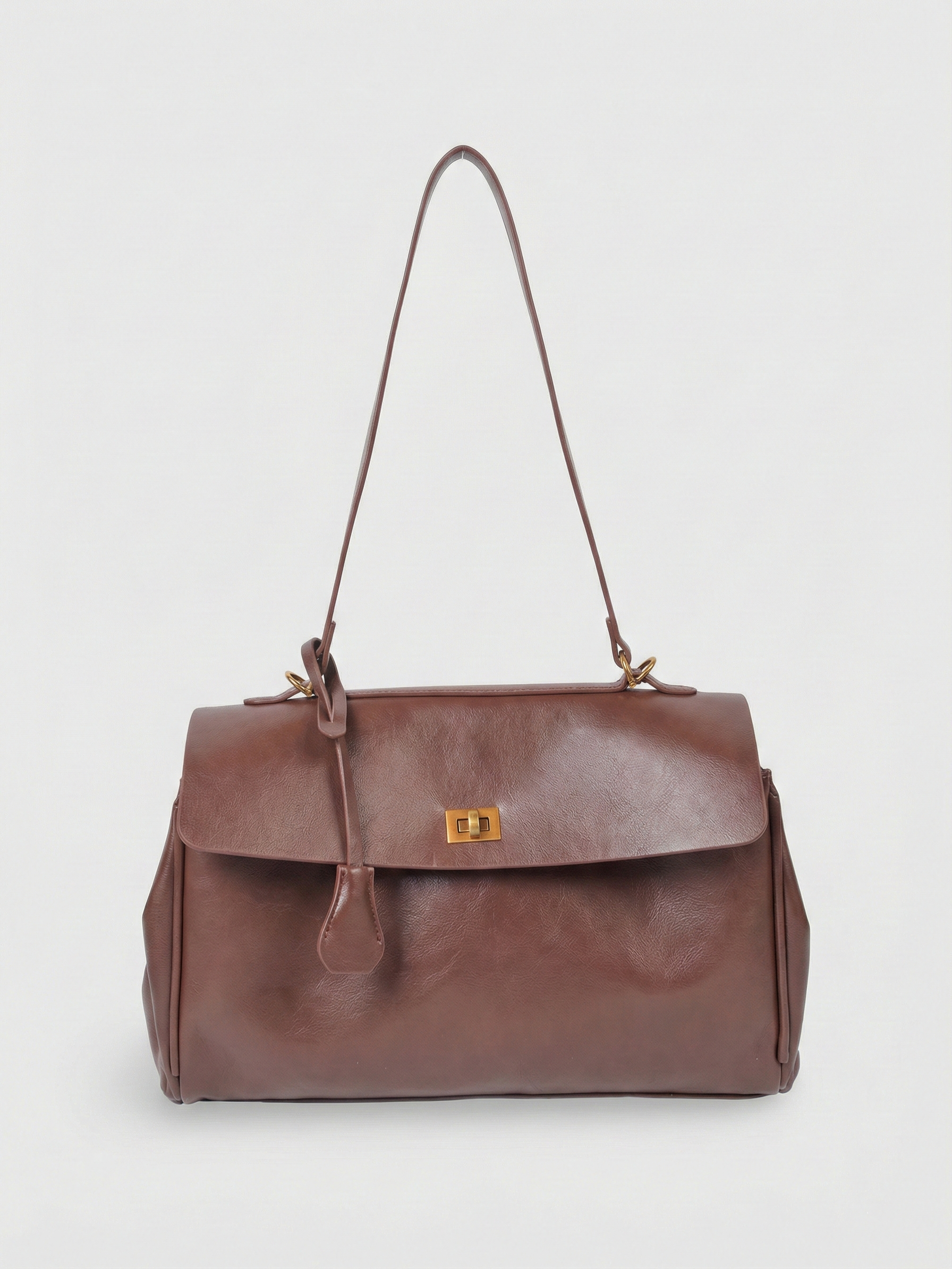 Brown leather shoulder bag with structured shape, flap closure and slim top handle, photographed on a light background