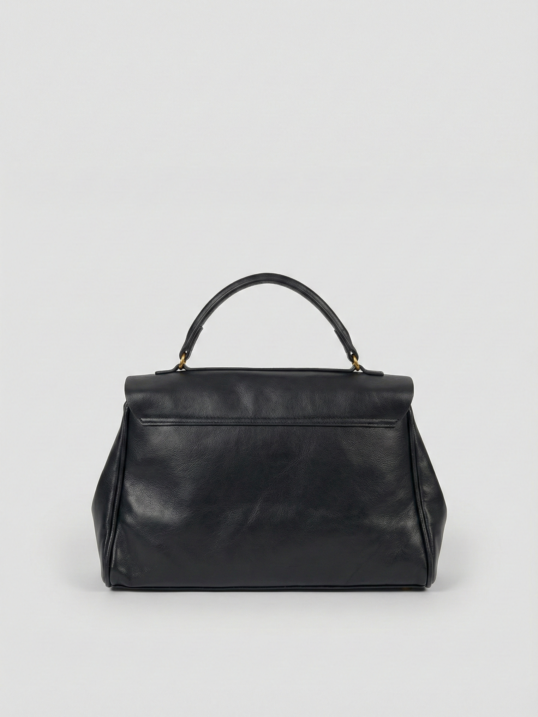 Black leather shoulder bag with structured shape, flap closure and slim top handle, photographed on a light background