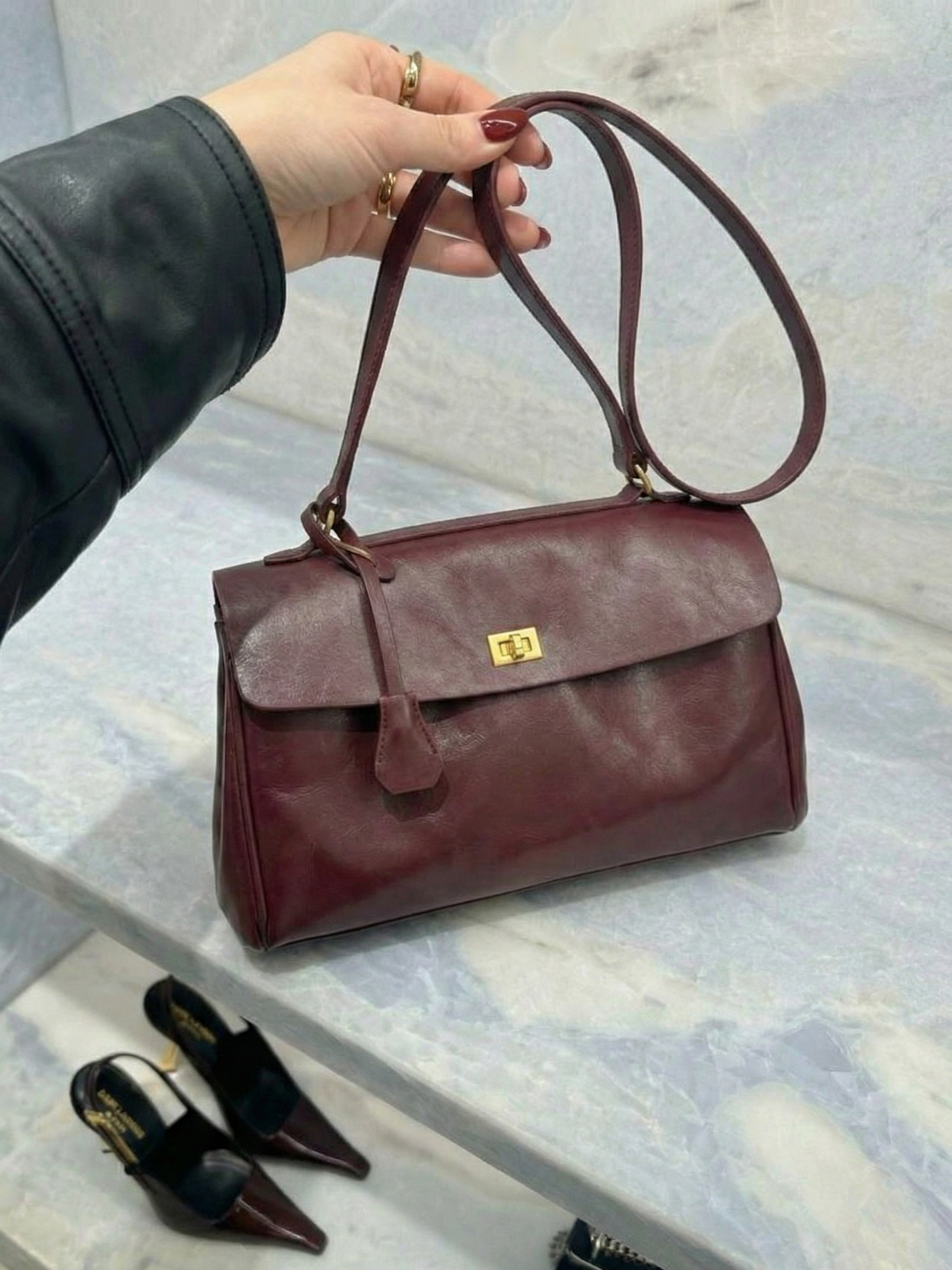 Burgundy leather shoulder bag with structured shape, flap closure and slim top handle, photographed on a light background