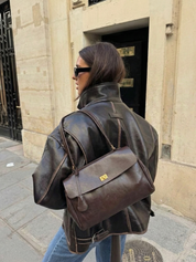 Dark brown leather shoulder bag with structured shape, flap closure and slim top handle, photographed on a light background