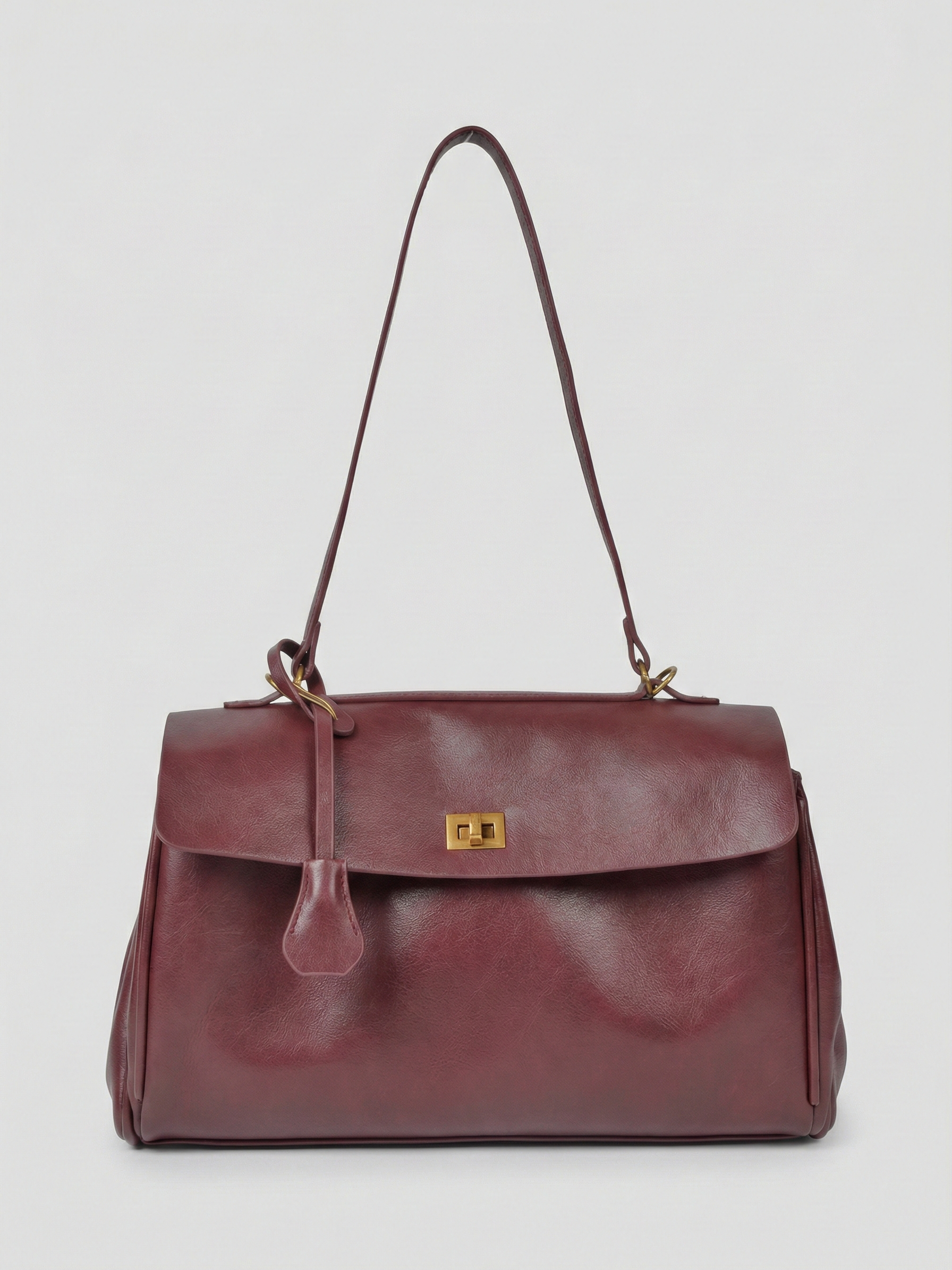 Burgundy leather shoulder bag with structured shape, flap closure and slim top handle, photographed on a light background