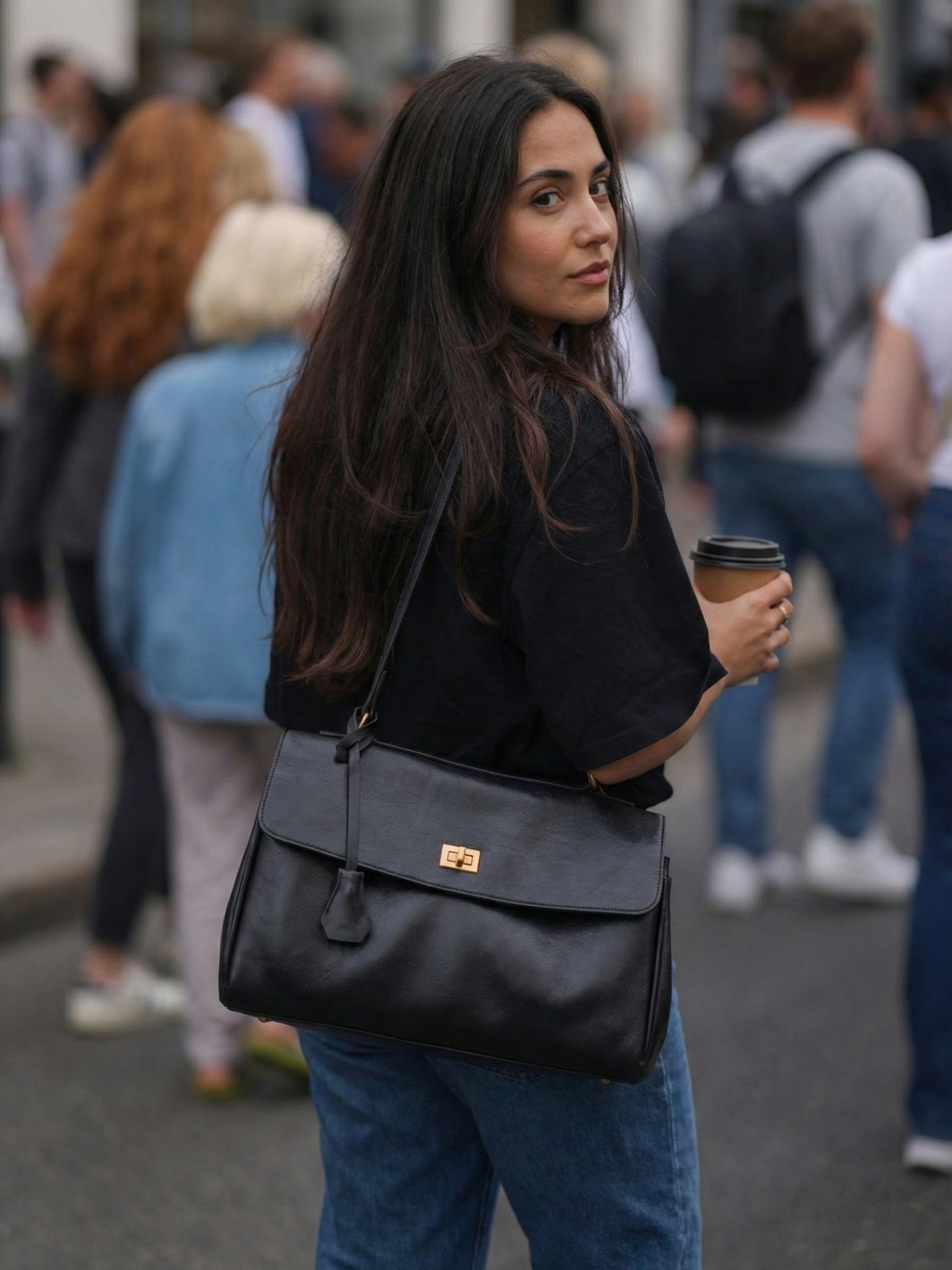 Black leather shoulder bag with structured shape, flap closure and slim top handle, photographed on a light background