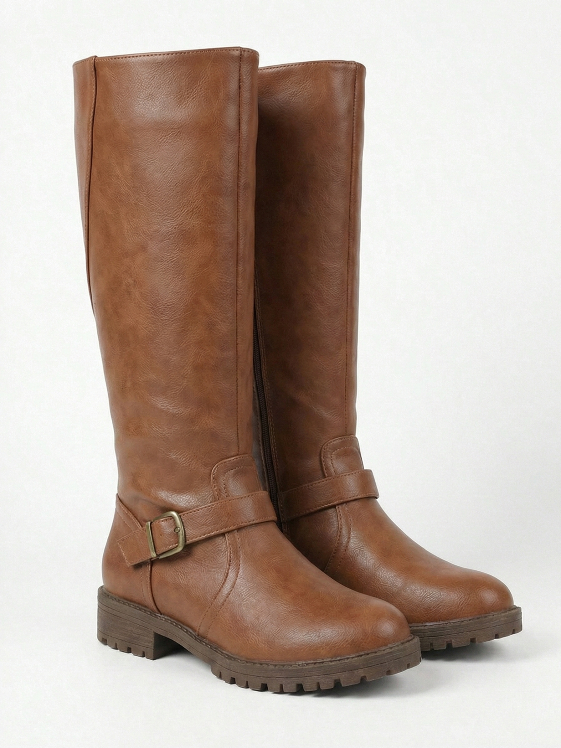 Brown knee-high leather-look boot with side buckle strap, round toe and chunky tread sole, minimalist studio white background.