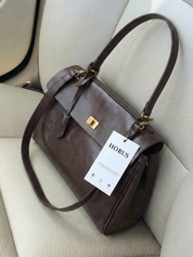 Dark brown leather shoulder bag with structured shape, flap closure and slim top handle, photographed on a light background
