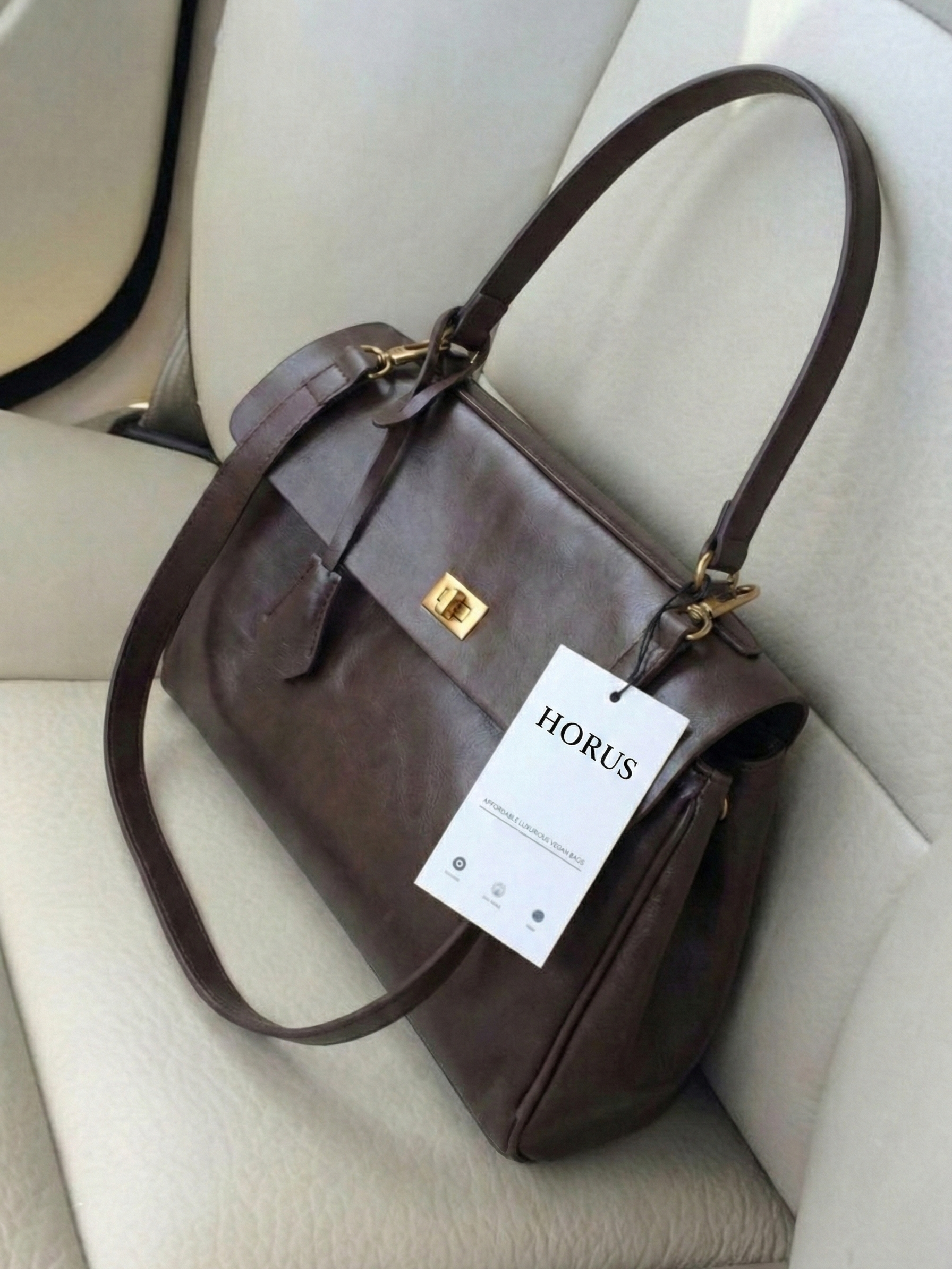 Dark brown leather shoulder bag with structured shape, flap closure and slim top handle, photographed on a light background