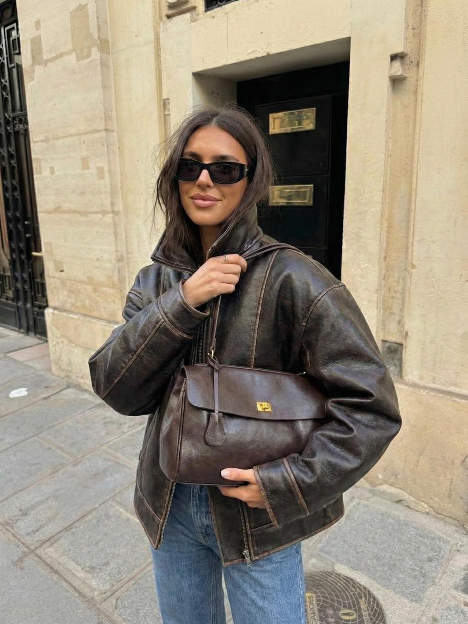 Dark brown leather shoulder bag with structured shape, flap closure and slim top handle, photographed on a light background