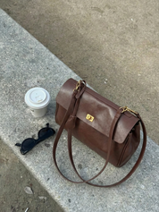 Brown leather shoulder bag with structured shape, flap closure and slim top handle, photographed on a light background