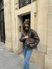 Dark brown leather shoulder bag with structured shape, flap closure and slim top handle, photographed on a light background