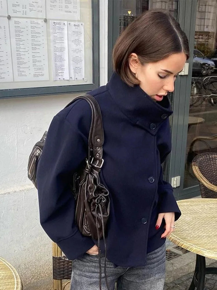 Black high-neck jacket with asymmetrical buttons and structured silhouette, featuring wide sleeves and a minimalist design for modern everyday styling.