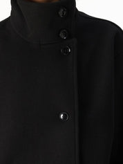 Black high-neck jacket with asymmetrical buttons and structured silhouette, featuring wide sleeves and a minimalist design for modern everyday styling.