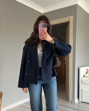 Navy double-breasted short jacket featuring a structured fit, wide lapel collar and clean tailoring. A versatile women’s jacket ideal for autumn and winter everyday wear.